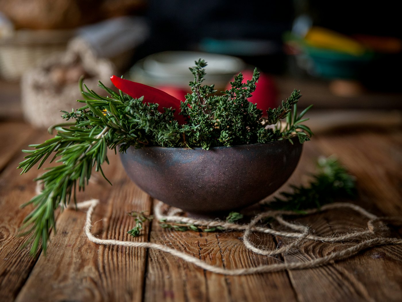 Fresh rosemary and thyme in a dark ceramic bowl on a weathered wooden table.